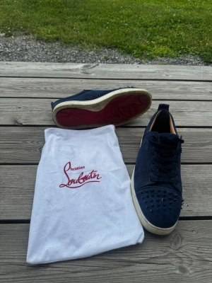 Christian Louboutin skor - Detaljer:  * Märke: Christian Louboutin * Färg: Mörkblå * Material: Mocka ovandel * Design: Dekorativa nitar * Signatursula: Röd undersula * Mellansula/sidokant: Vit * Skick: Acceptabelt begagnat skick * Normal användning med visst slitage förekommer  Skick:  * Skorna är i acceptabelt skick och fungerar som de ska. * Tecken på användning finns, vilket är naturligt för begagnade skor. * En grov rengöring kommer att utföras innan skorna till köparen.