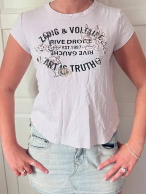 Vit t-shirt Zadig & Voltaire broderad - Vit t-shirt från Zadig & Voltaire med coolt broderat motiv framtill och text i svart. T-shirten har korta ärmar och rund halsringning. Materialet känns mjukt och skönt, troligen bomull. Perfekt för dig som gillar edgy detaljer och streetstyle.