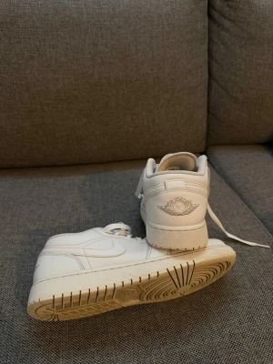 Vita Air Jordan 1 Low sneakers - Säljer ett par klassiska vita Air Jordan 1 Low sneakers från Nike. Skorna är helt vita i läder med den ikoniska Air Jordan-loggan på hälen och Nike swoosh på sidan. Tidlös design med lågt skaft och bekväm sula. Perfekta för dig som gillar clean och stilren look.