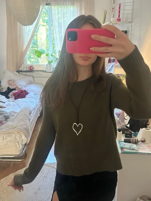 Olivgrön stickad tröja - Mysig olivgrön stickad tröja med rund hals och långa ärmar. Tröjan har en enkel, rak passform och ribbade muddar vid ärmslut och nederkant. Perfekt att matcha med kjol eller jeans för en avslappnad look.
