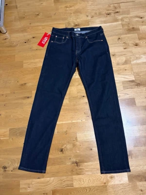 Levi's 501 mörkblå raka jeans - Klassiska Levi's 501 jeans i mörkblå denim med raka ben och knappgylf. Snygga kontrastsömmar och femficksmodell. Perfekta för dig som gillar tidlös stil och vill ha ett par jeans som funkar till allt.