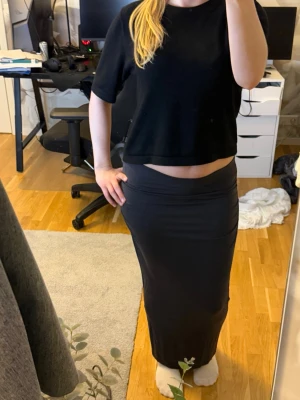 Svart långkjol i stretchigt material - Säljer en svart långkjol med tight passform. Kjolen är enkel och stilren utan mönster eller detaljer, perfekt för dig som gillar minimalistisk stil. Materialet känns mjukt och stretchigt vilket gör den bekväm att bära hela dagen.