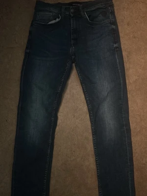 Mörkblå slim fit jeans från Blend - Snygga mörkblå slim fit jeans från Blend med klassisk femficksdesign och slitna detaljer. Jeansen har normal midja, dragkedjegylf och kontrastsömmar. Perfekta för en avslappnad och trendig look.