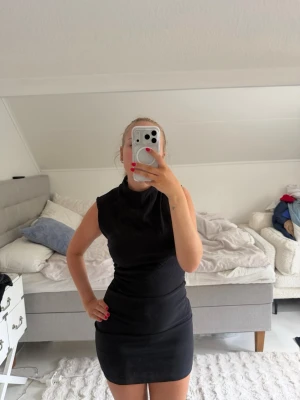 Svart ärmlös kortklänning - Säljer en svart, tight och ärmlös kortklänning med hög hals. Klänningen har en enkel och stilren design utan synliga detaljer eller mönster. Perfekt för dig som gillar minimalistisk stil.
