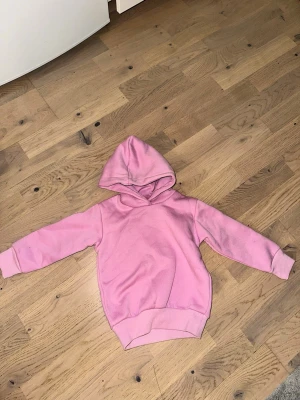 Rosa hoodie med huva - En enkel och snygg rosa hoodie med huva och långa ärmar. Hoodien har breda muddar vid ärmslut och nederkant för en skön passform. Perfekt för dig som gillar en avslappnad och casual stil. Materialet känns mjukt och bekvämt mot huden.Rosa hoodie med huva