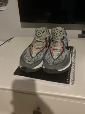 Nike Gt cuts 2 - Snygga Nike ZoomX Invincible Run Flyknit sneakers med grå och vita nyanser, svarta detaljer och inslag av blått och rött. Ovandelen är i ventilerande mesh och sulan är tjock och dämpande för extra komfort. Perfekta för dig som gillar sportig stil.