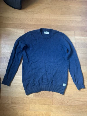 Mörkblå stickad tröja från Dobber - Snygg mörkblå stickad tröja från Dobber med rund halsringning och ribbade muddar vid ärmslut och nederkant. Enkel och stilren design som passar perfekt till jeans eller chinos. Tillverkad i mjukt material för skön känsla.