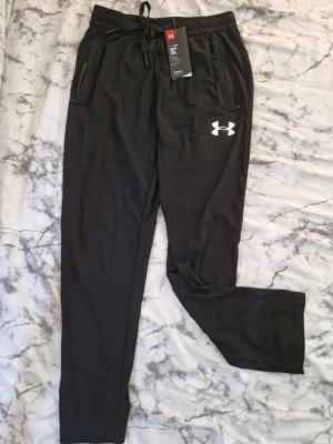 Svarta sommar byxor från Under Armour - Svarta mjukisbyxor från Under Armour med dragsko i midjan och två sidofickor med dragkedja.