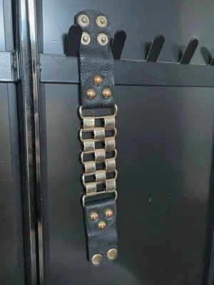 Svart läderarmband med metallkedja - Coolt svart armband i läder med bred metallkedja i silverfärg och nitar i mässing. Armbandet har tryckknappar för enkel stängning och en robust, edgy design som passar perfekt till streetwear eller rockig stil. Min mammas gamla från 2000s så vet inte märket