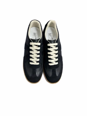 Svarta Maison Margielas  - Snygga svarta sneakers med vita snören och beige sula. Skorna har en klassisk låg siluett och är tillverkade i en mix av mocka och läder. Perfekta för dig som gillar stilrena och tidlösa sneakers med en sportig vibe.