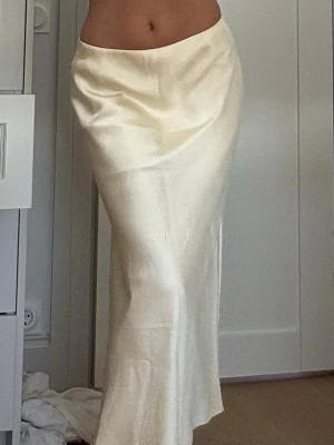 Lång gul satinkjol - Säljer en lång, elegant gul kjol i satinliknande material. Kjolen har en slät och glansig yta som ger ett lyxigt intryck och sitter högt i midjan. Perfekt för dig som gillar minimalistisk och stilren look.