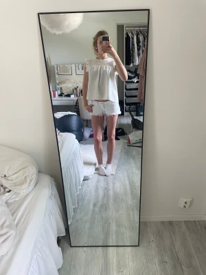 Vit blus med spetsdetaljer - Söt vit blus med volangärmar och spets upptill. Blusen har en luftig passform och är perfekt för varma dagar. Den är ärmlös och har en rund halsringning. Passar till både jeans och kjol för en fräsch look.