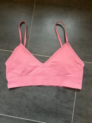 Rosa ribbad sporttopp från Aim’n - Säljer en rosa ribbad sporttopp från Aim’n. Toppen har justerbara smala axelband, V-ringning och stretchigt material. Enkel och stilren design med vaddering som går att ta ur. 