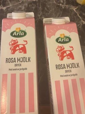 Arla Rosa Mjölk Jordgubb 1L - Två förpackningar Arla Rosa mjölk dryck. Kartongerna är vita med rosa ränder och har en rosa ko på framsidan. Varje förpackning rymmer 1 liter och har skruvkork. Perfekt för dig som gillar smaksatt mjölkdryck. Finn