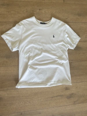 Vit t-shirt från Polo Ralph Lauren - Klassisk vit t-shirt från Polo Ralph Lauren med den ikoniska broderade loggan på bröstet. T-shirten har rund hals, korta ärmar och är gjord i mjuk bomull för en skön och avslappnad stil. Passar även om du har S