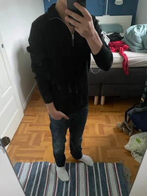 Svart halvzip tröja - Säljer en svart långärmad tröja med halv dragkedja i halsen. Tröjan har en enkel och stilren design, perfekt att matcha med jeans eller andra byxor. Materialet ser mjukt och bekvämt ut, och passformen är rak och avslappnad.