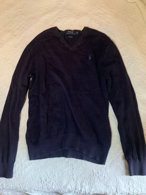 Mörkblå stickad tröja Polo Ralph Lauren - Mörkblå stickad tröja från Polo Ralph Lauren i 100% bomull. Klassisk v-ringning och lång ärm. Tröjan har den ikoniska broderade loggan på bröstet och ribbade muddar vid ärmslut och nederkant. Perfekt för en stilren och avslappnad look. Tycker att tröjan verkar vara mer en storlek s än m när den är på. 