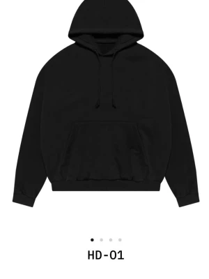 Svart oversized hoodie från Yeezy HD-01 - Säljer en svart oversized hoodie med stor huva och dragsnören. Hoodien har en klassisk känguruficka framtill och ribbade muddar vid ärmslut och nederkant. Perfekt för en avslappnad och trendig streetwear-look. Storlek 2 ungefär medium. Använd hemma någon gång bara.