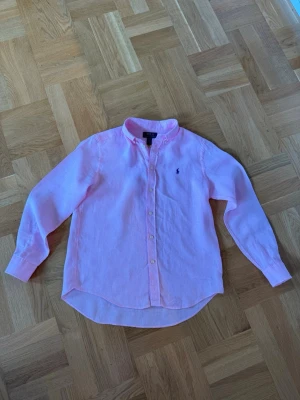 rosa Ralph lauren linneskjorta - Säljer en ljusrosa skjorta från Ralph Lauren i 100% linne.  Passformen är regular och storleken är i L i barnstorlekar vilket motsvarar S i vuxenstorlekar. Varan är i helt nytt skick. Använt en sommar och växt ur den och nu är den för liten och därför säljer jag den. Pris kan diskuteras!