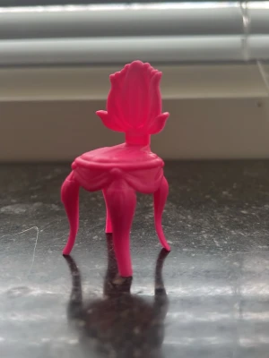 Liten rosa leksaksstol i plast - En liten rosa leksaksstol i plast med dekorativ rygg och böjda ben. Stolen har en fantasifull design som påminner om en blomma och passar perfekt till dockhus eller som dekoration.