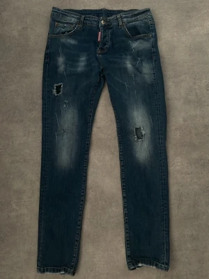 Blå slitna jeans från Dsquared2 - Snygga blå jeans från Dsquared2 med slitningar och hål på benen för en cool, avslappnad look. Klassisk femficksmodell med knappgylf och tydliga detaljer. Perfekta för dig som gillar streetstyle och trendiga outfits. storlek 48 ( M/S )