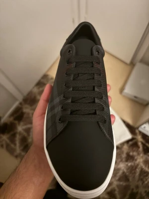 Burberry svart-rutiga sneakers - Snygga sneakers från Burberry i svart med klassiskt rutmönster och vita sulor. Skorna har svarta skosnören, rund tå och detaljer i läder. Perfekta för dig som vill ha en stilren och exklusiv look med en touch av brittisk design. (Pris kan diskuteras)