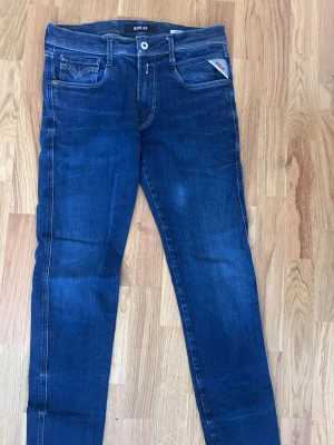Mörkblå Anbass  jeans från Replay - Snygga mörkblå jeans från Replay med klassisk femficksmodell och kontrastsömmar. Jeansen har en rak passform och detaljer som logotyp på myntfickan. Perfekta till en avslappnad streetstil.