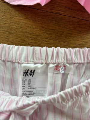2-pack pyjamasshorts från H&M XS - Två par pyjamasshorts från H&M i storlek XS. Ena paret är ljusrosa och det andra är vitt med tunna rosa ränder. Båda har resår i midjan och dragsko för skön passform. Perfekta för chill dagar hemma eller som sovplagg.