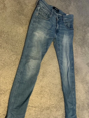 Ljusblå Anbass jeans från Replay - Säljer ett par ljusblå jeans från Replay med klassisk femficksdesign och snygga slitningar. Jeansen har normal midja och smal passform hela vägen ner. Perfekta för dig som gillar en avslappnad men trendig stil.