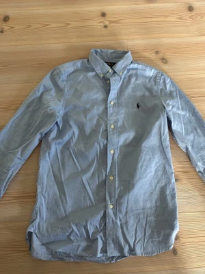 Polo Ralph Lauren skjorta - Klassisk ljusblå skjorta från Polo Ralph Lauren i slim fit-modell. Skjortan har knappar framtill, button down-krage och den ikoniska broderade loggan på bröstet. Tillverkad i mjuk bomull och har långa ärmar. Väldigt fint skick, inte använd mycket och den är i storlek xs. Hör av er vid funderingar!