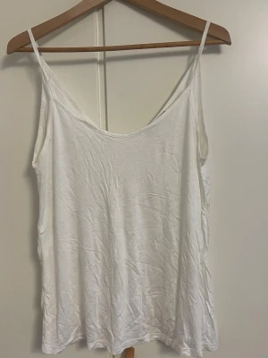 Vit linnetopp med tunna axelband - En enkel och stilren vit linnetopp med tunna axelband och rundad urringning. Perfekt till sommaren och lätt att matcha med olika outfits. Tillverkad i mjuk bomull för en skön känsla.