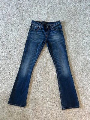 Blåa Nudie Bootcut Jeans Narrow Boot Storlek W27 L32 - Mycket fina Nudie jeans i blå färg | Jeansen är i mycket bra skick och sparsamt använda. |  Äkta som allt annat jag säljer! ✅ |  Storlek: W27 | Skick: Mycket Bra Skick  - liten fläck på baksidan av ena byxbenet (SE SISTA BILD)| Färg: Blå | Märke: Nudie Modell: Jeans |   Hör gärna av dig vid frågor så svarar jag så fort jag kan! 😁 |  (SKU - 184)