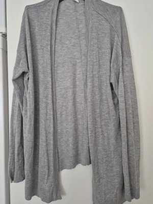 Cardigan - Ljusgrå cardigan med öppen front och långa ärmar. Mjuk och tunn stickad kvalitet som faller snyggt. Perfekt att slänga över en t-shirt eller topp för en chill look. Enkel design utan knappar eller fickor.