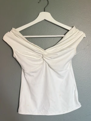Vit offshoulder topp med twist - Trendig vit offshoulder topp med twistad detalj framtill. Toppen har en smickrande v-ringning och är ärmlös med breda axelband som sitter nedanför axlarna. 💕☺️