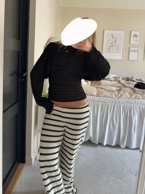 Svart ribbad långärmad topp - Säljer en svart ribbad topp med lång ärm och tight passform. Toppen har en lätt croppad längd och är gjord i ett stretchigt syntetmaterial som sitter snyggt på kroppen. Perfekt att styla med både jeans och kjol.