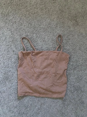 Beige croppad linnetopp - Storleken är S men passar mer som XS. Säljer en enkel och stilren beige croppad linnetopp med tunna axelband. Toppen har en rak skärning och är perfekt för varma dagar. Materialet känns mjukt och lätt mot huden.