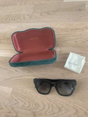 Äkta Gucci solglasögon - Äkta Gucci solglasögon i modellen GG0029S. Svarta bågar med silver detaljer. Kommer med original fodral + dust. Ordinarie pris ligger omkring 2 600 kr.