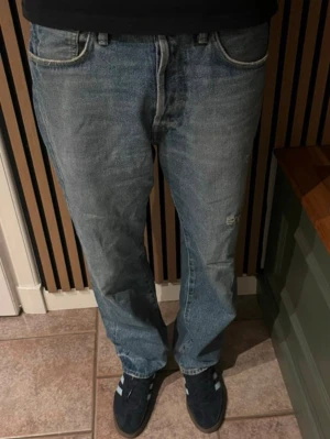 Blå raka jeans från Acne Studios - Säljer ett par klassiska blå jeans från Acne Studios med rak passform och normal midja. Jeansen har en snygg tvättad look och subtila slitningar på låret. Tillverkade i denim med Acne Studios läderpatch bak i midjan. Storleken är 29/32 och skicket är 8/10! Nypris cirka 4500kr