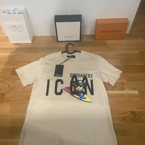 Beige t-shirt från Dsquared2 - Helt ny och oanvänd Snygg beige t-shirt från Dsquared2 i storlek small med trycket 'ICON' och en färgglad grafik på framsidan. Perfekt för en stilren och modern look.