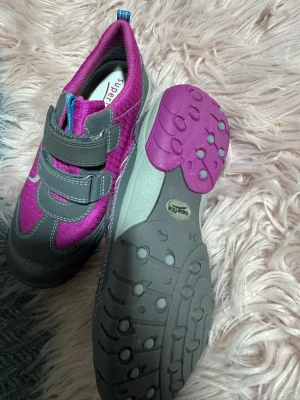 Lila sneakers från Superfit med kardborre - Oanvända skor från xxl.Snygga sneakers från Superfit i lila och grått med vita detaljer. Skorna har två praktiska kardborreband och en robust sula med lila och grå partier. Ovandelen är i textil och syntet, perfekt för en aktiv vardag.