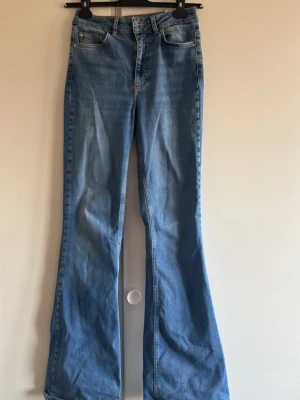 Ljusblå utsvängda jeans - Snygga ljusblå jeans med utsvängda ben och klassisk femficksdesign. Jeansen har hög midja och är tillverkade i denim med lätt tvättad look. Perfekta för dig som gillar retrostil och vill ha ett par bekväma och trendiga jeans.