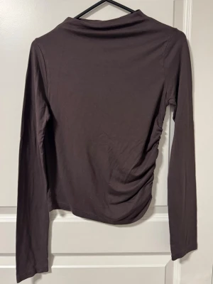 Mörkbrun långärmad topp - En enkel mörkbrun långärmad topp med rak passform på ena sidan och på den andra är en rynksömn.
