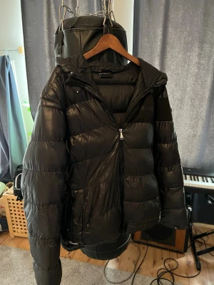 Alessandro zavetti jacka - Säljer en svart pufferjacka med huva och dragkedja framtill. Jackan har en klassisk quiltad design och är vadderad för extra värme. Perfekt för kalla vinterdagar och har en stilren look som passar till det mesta. Skriv vid funderingar och frågar sp ska jag försöka svara så snabbt jag kan