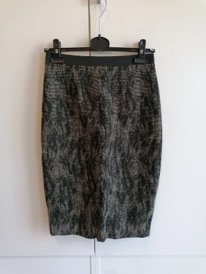 Svartmönstrad pennkjol med dragkedja - Snygg svart och beige pennkjol med abstrakt mönster och hel dragkedja bak. Kjolen har en smal passform och är perfekt för dig som gillar stilrena plagg med en twist. Resår i midjan för extra komfort.