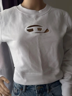 Vit långärmad topp med cut-out - Cool vit långärmad topp med unik cut-out detalj framtill. Rund halsringning och ribbade muddar. Perfekt att matcha med jeans för en avslappnad look. Materialet känns som bomull och polyester.