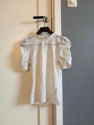 Vit spetsblus med puffärm - Supersöt vit blus i spets med puffiga korta ärmar. Blusen har ett blommigt spetsmönster.
