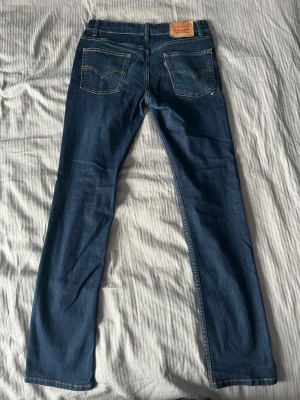 Levi's blå raka jeans - Slim modell. Storlek 16a, sitter som 30x32. Säljer ett par klassiska blå jeans från Levi's med raka ben och femficksmodell. Jeansen har kontrastsömmar, läderpatch bak i midjan och är tillverkade i slitstark denim. Perfekta för en avslappnad och tidlös stil.