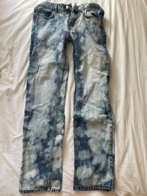 Acid wash jeans från Nelly - Säljer ett par snygga lågmidjade acid wash jeans från Nelly med rak passform. Jeansen har klassisk femficksdesign och coolt mönster i blått och vitt. Perfekta för dig som vill sticka ut med din stil. Storlek 36 men passar också på någon mer storlek 34