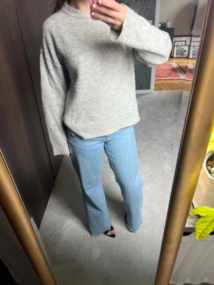 Grå stickad tröja med vid ärm - Mysig grå stickad tröja med rund hals och långa vida ärmar. Tröjan har en enkel och clean design med ribbade muddar vid ärmslut och nederkant. Lite nopprig men går enkelt att ta bort
