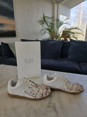 Maison Margiela skor med färgstänk - Unika vita skor från Maison Margiela med färgstänk i blått, gult, rött och svart. Skorna är helt nya, endast testade men passade tyvärr ej. Har tillbehör samt kvitto 🧾. Hör av er vid minsta fundering!